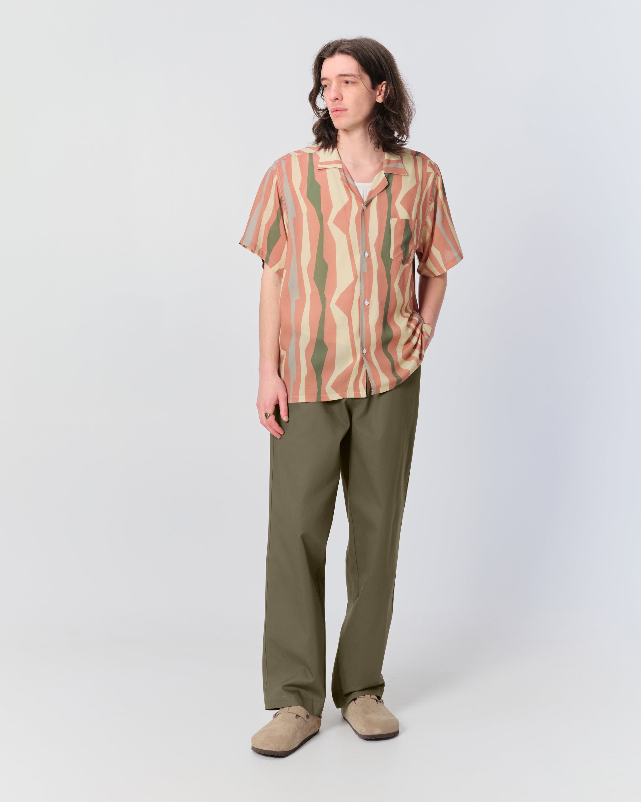 Male model wearing olive green herringbone drawstring pants with geometric striped pattern camp shirt