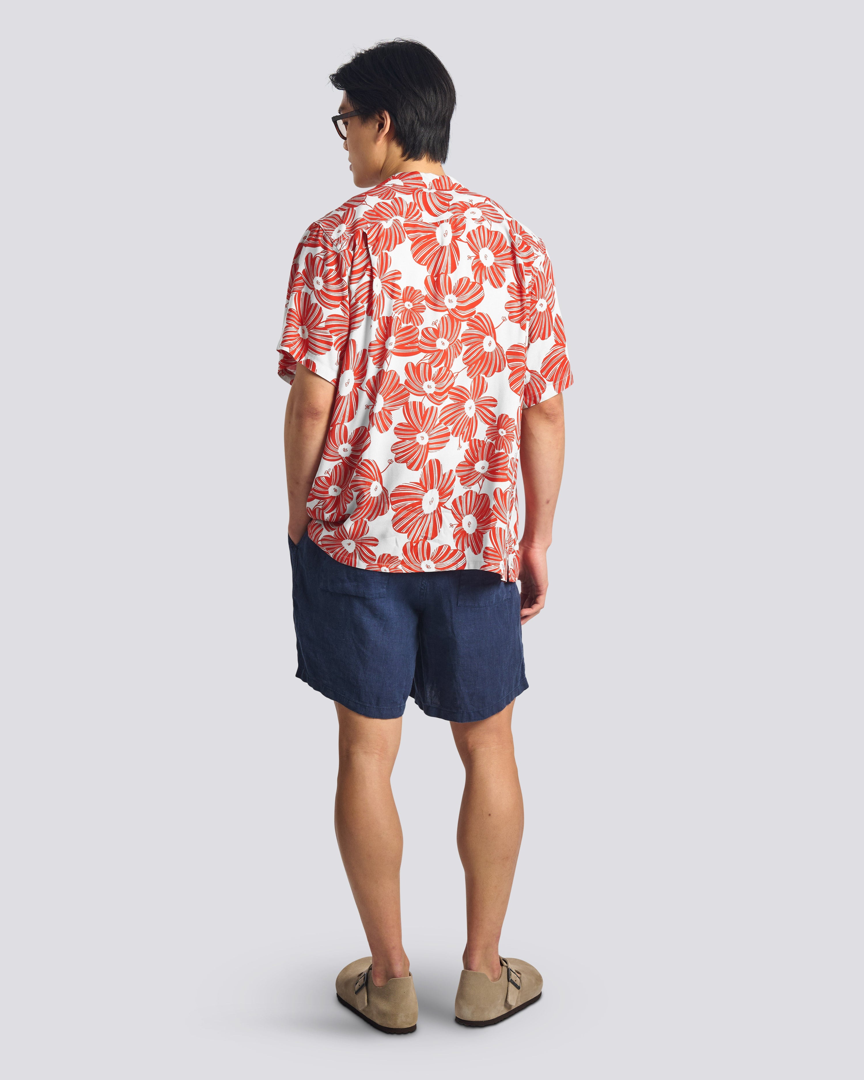Person wearing a red and white floral shirt and navy shorts on a light gray background