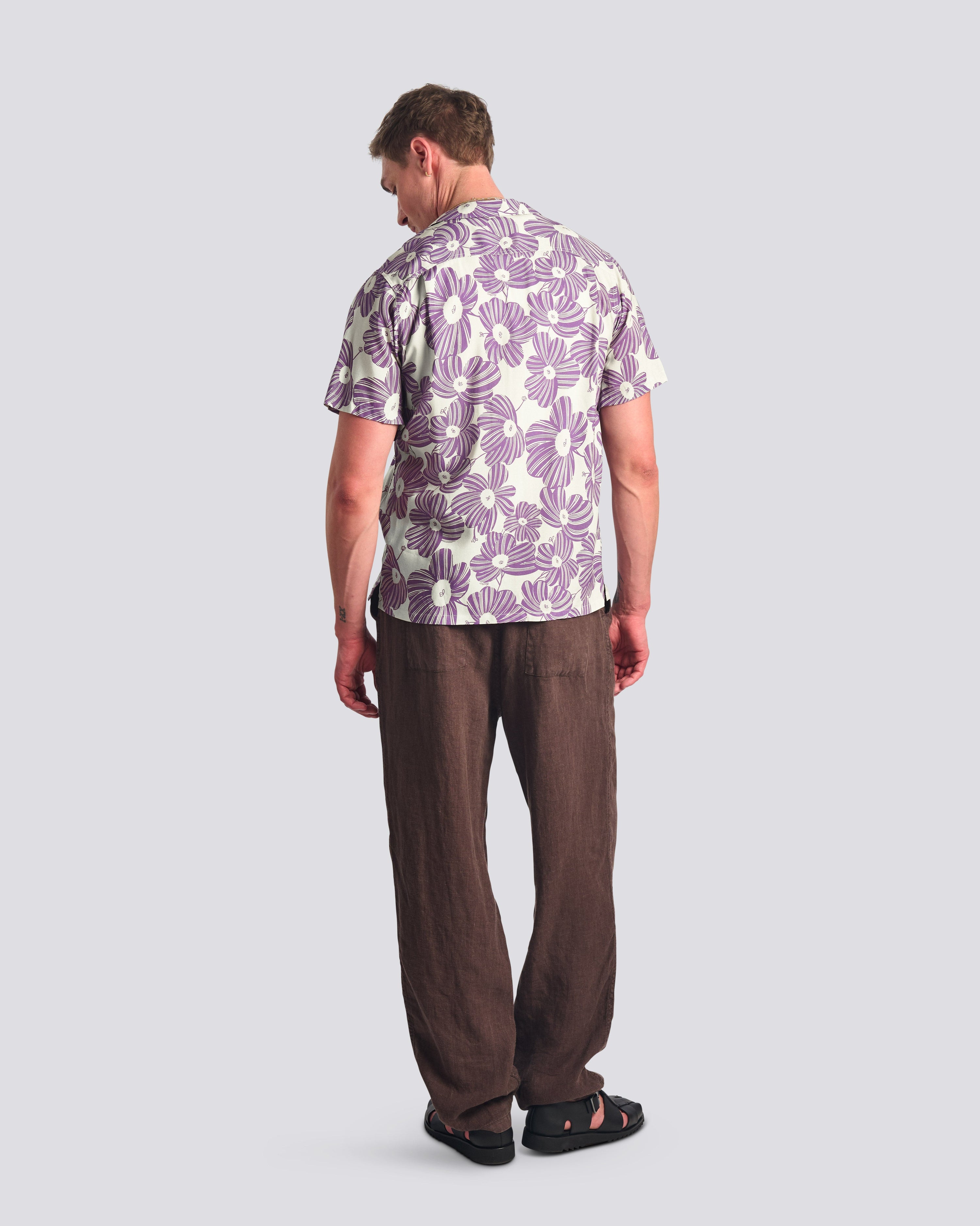 Man wearing a patterned shirt and brown pants on a light gray background