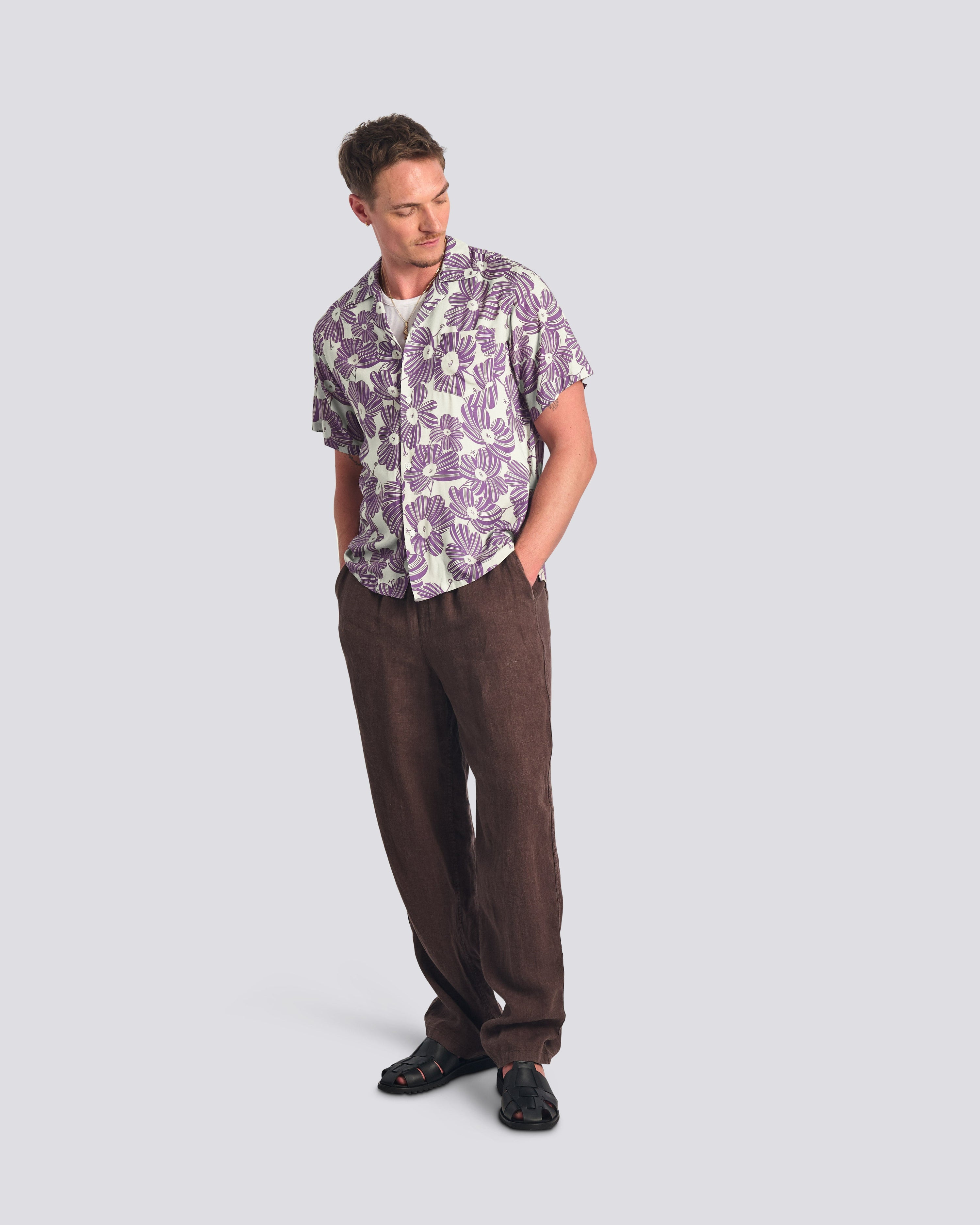 Man wearing a patterned shirt and brown pants on a light gray background