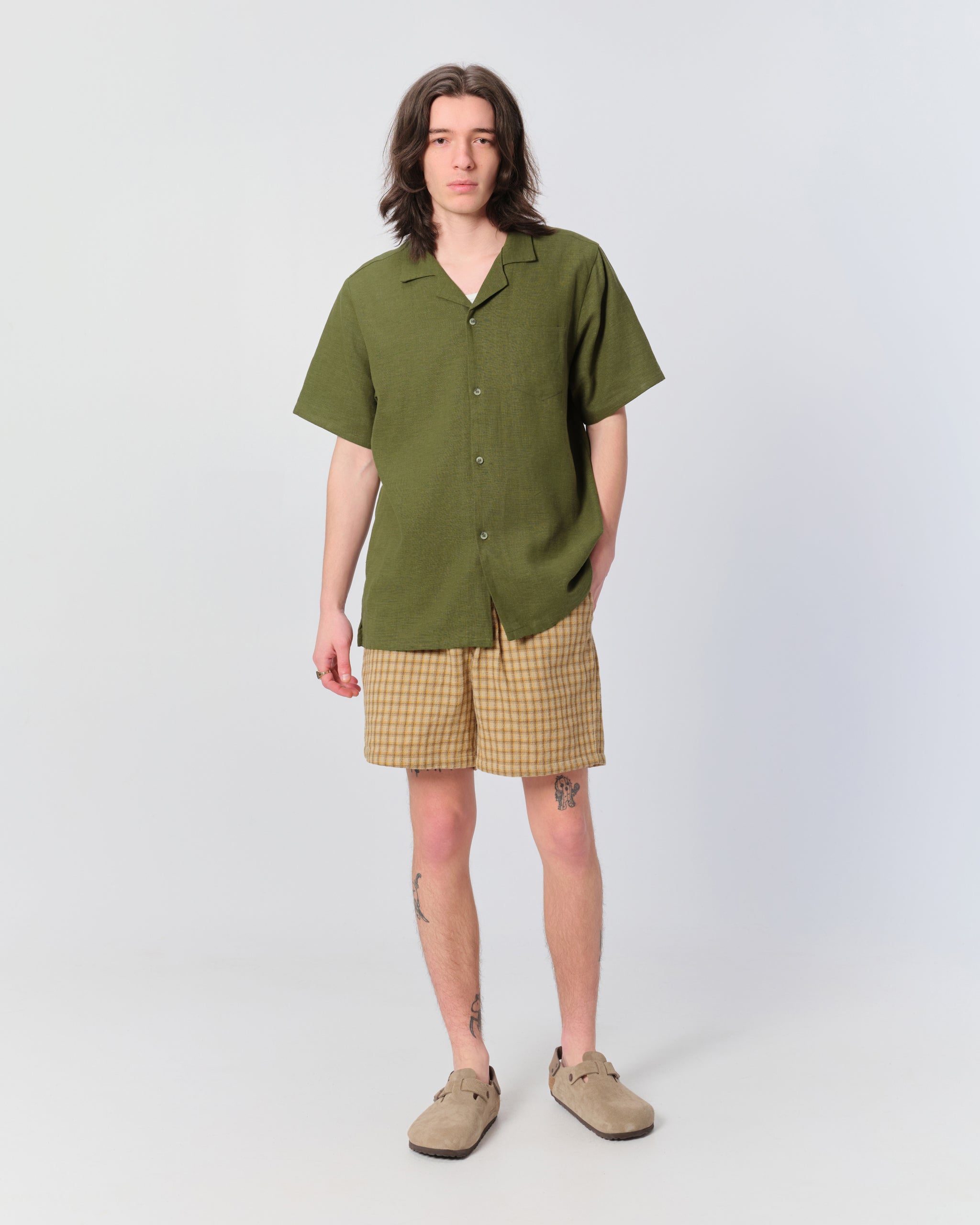 Male model wearing Bather men's brown drawstring shorts with checker plaid pattern and olive green camp shirt