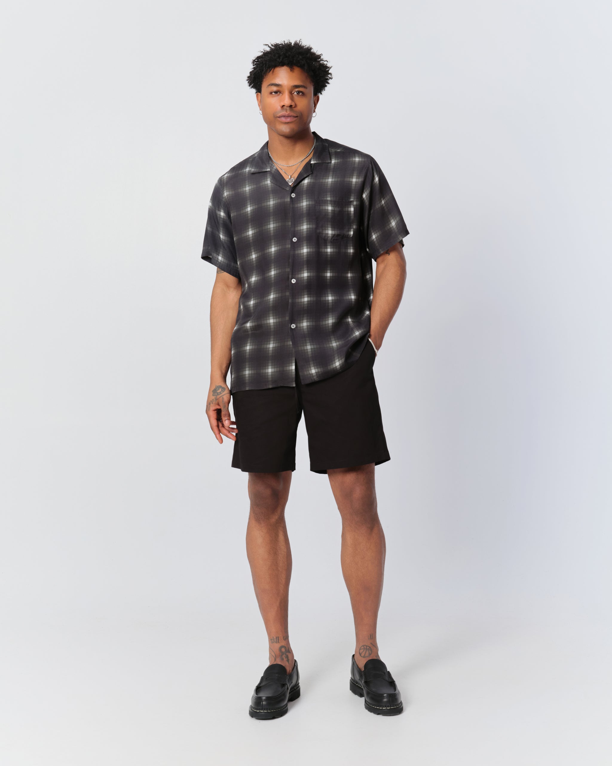 Male model wearing black and white patterned camp shirt and black shorts