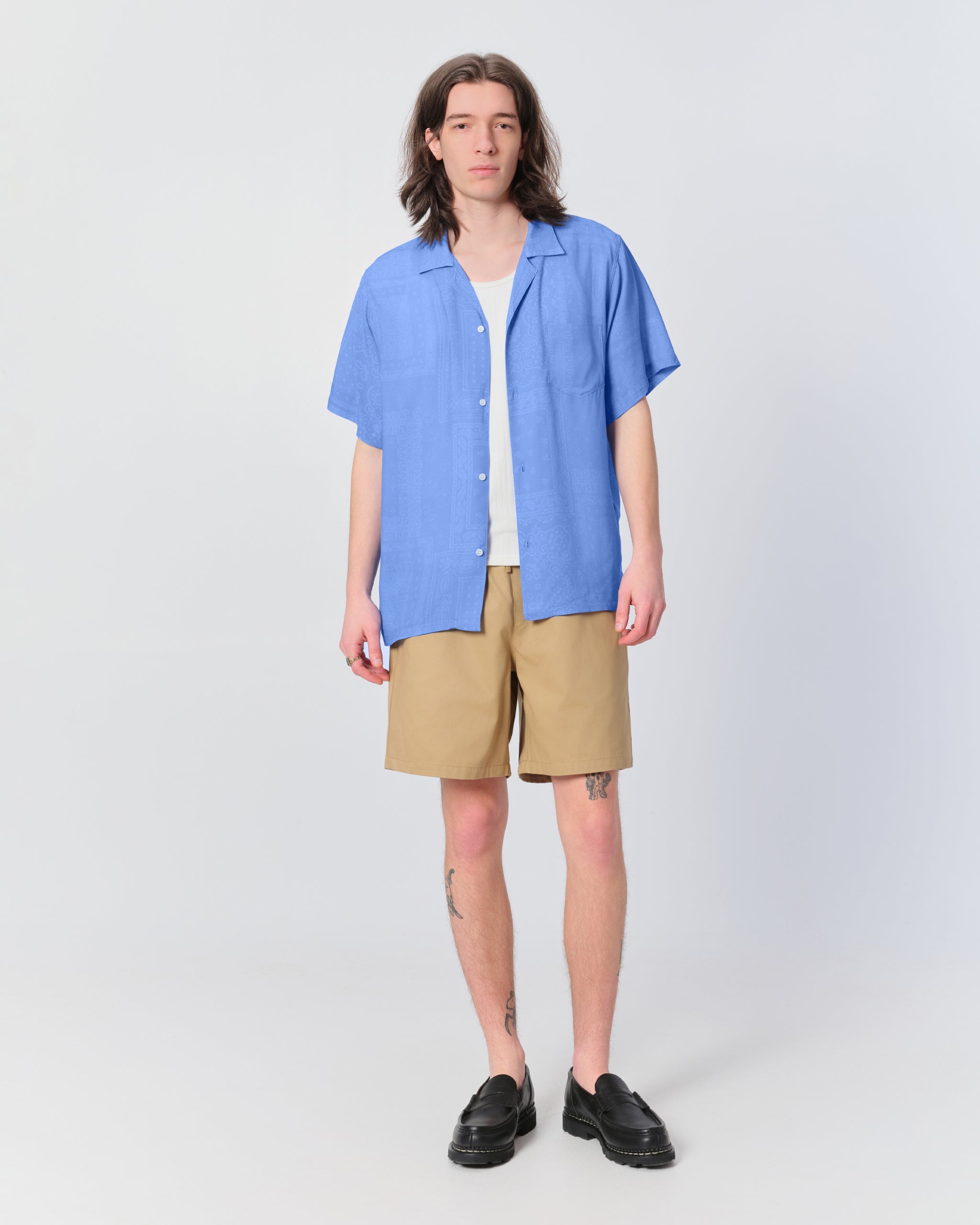 man wearing blue shirt with bandana print standing with khaki shorts on