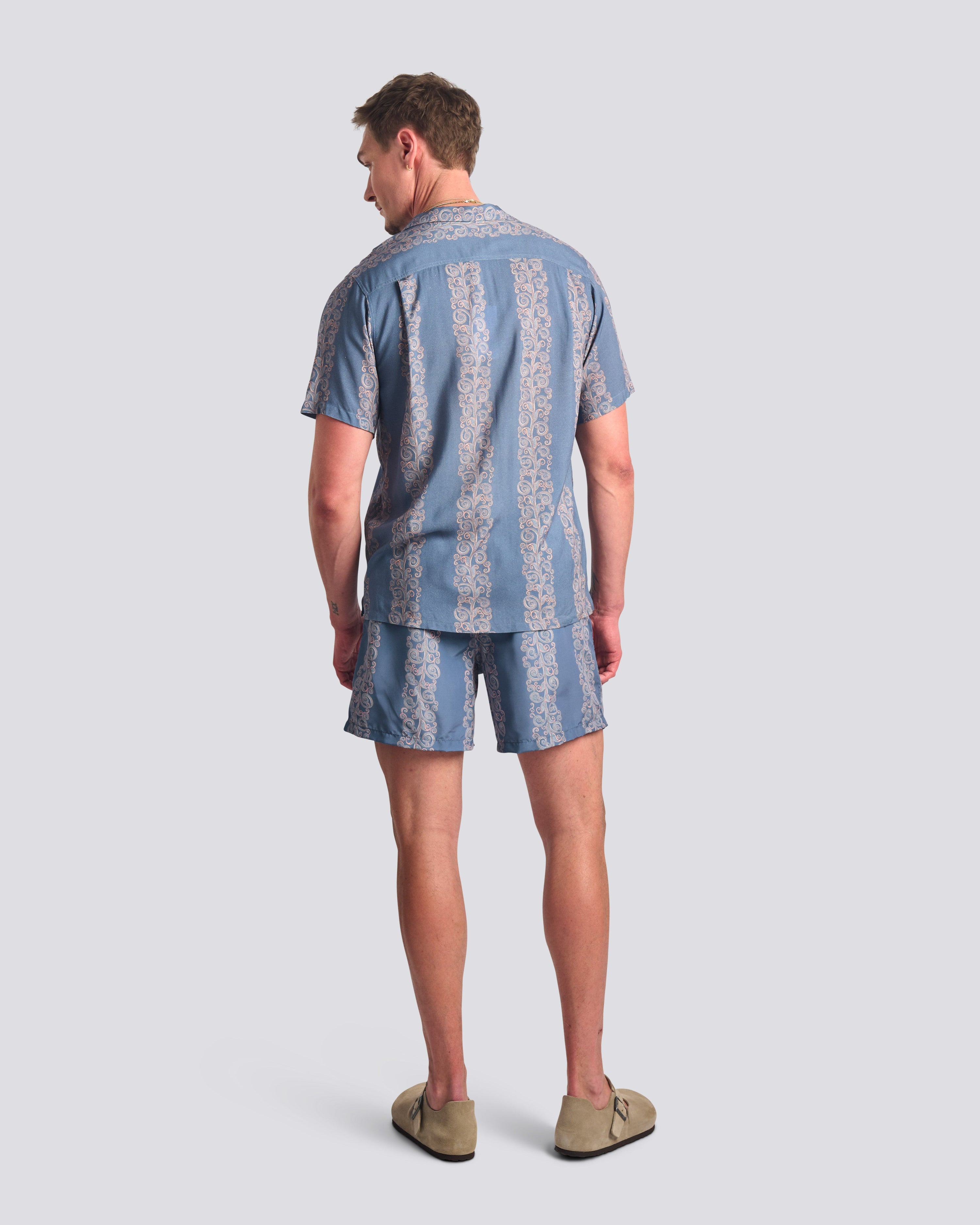 Man wearing a blue patterned shirt and shorts set on a light gray background