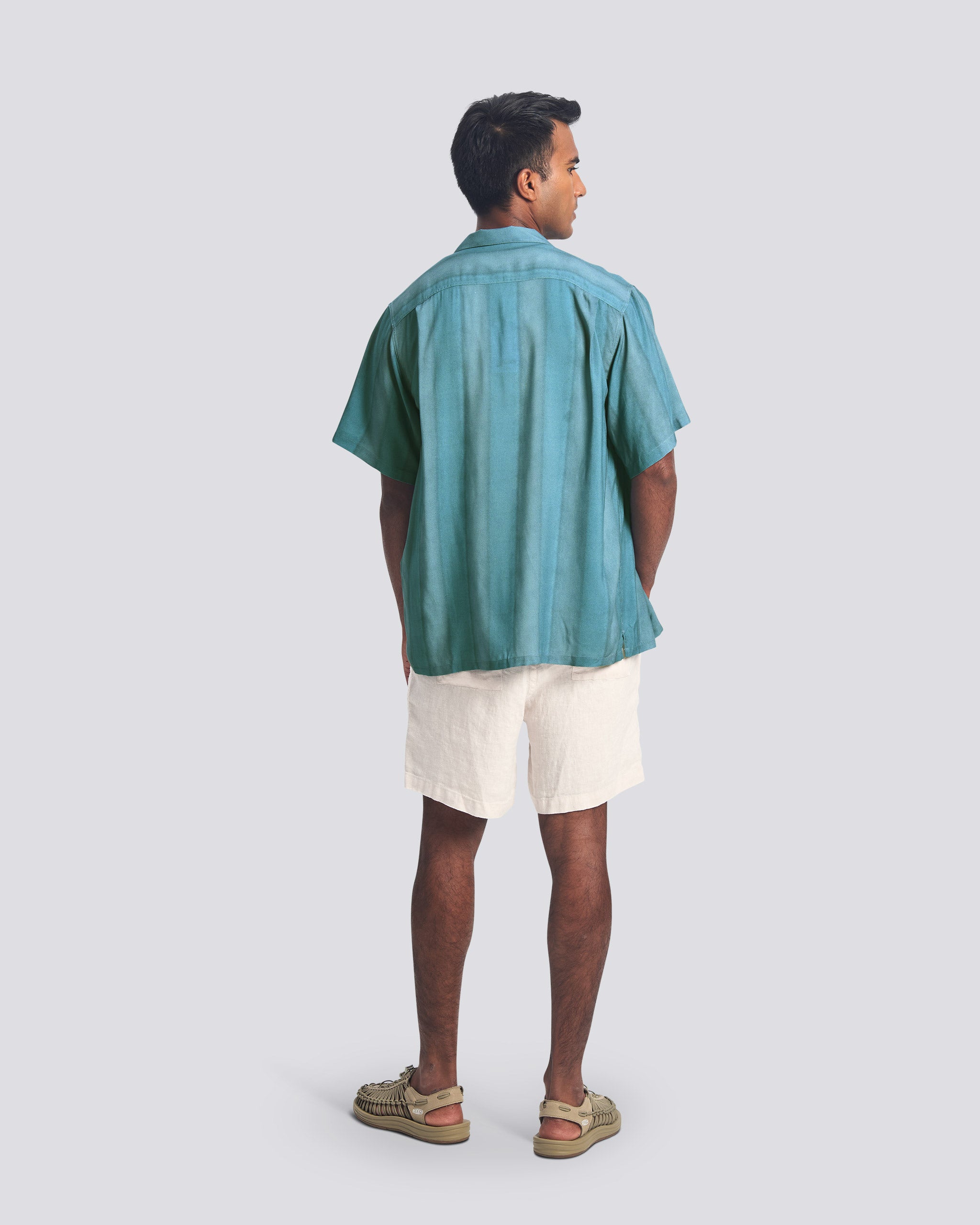 Man wearing a teal shirt and white shorts on a light gray background