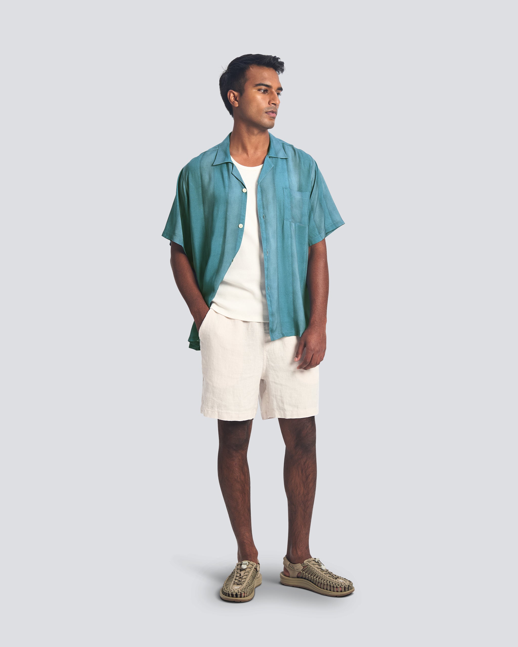 Man wearing a teal shirt, white shorts, and brown shoes on a light gray background