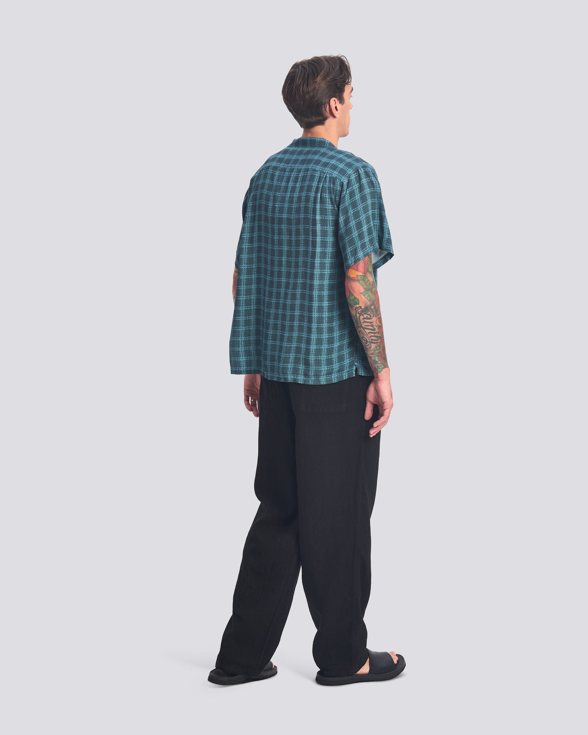 man wearing tartan shirt and black pants walking from behind