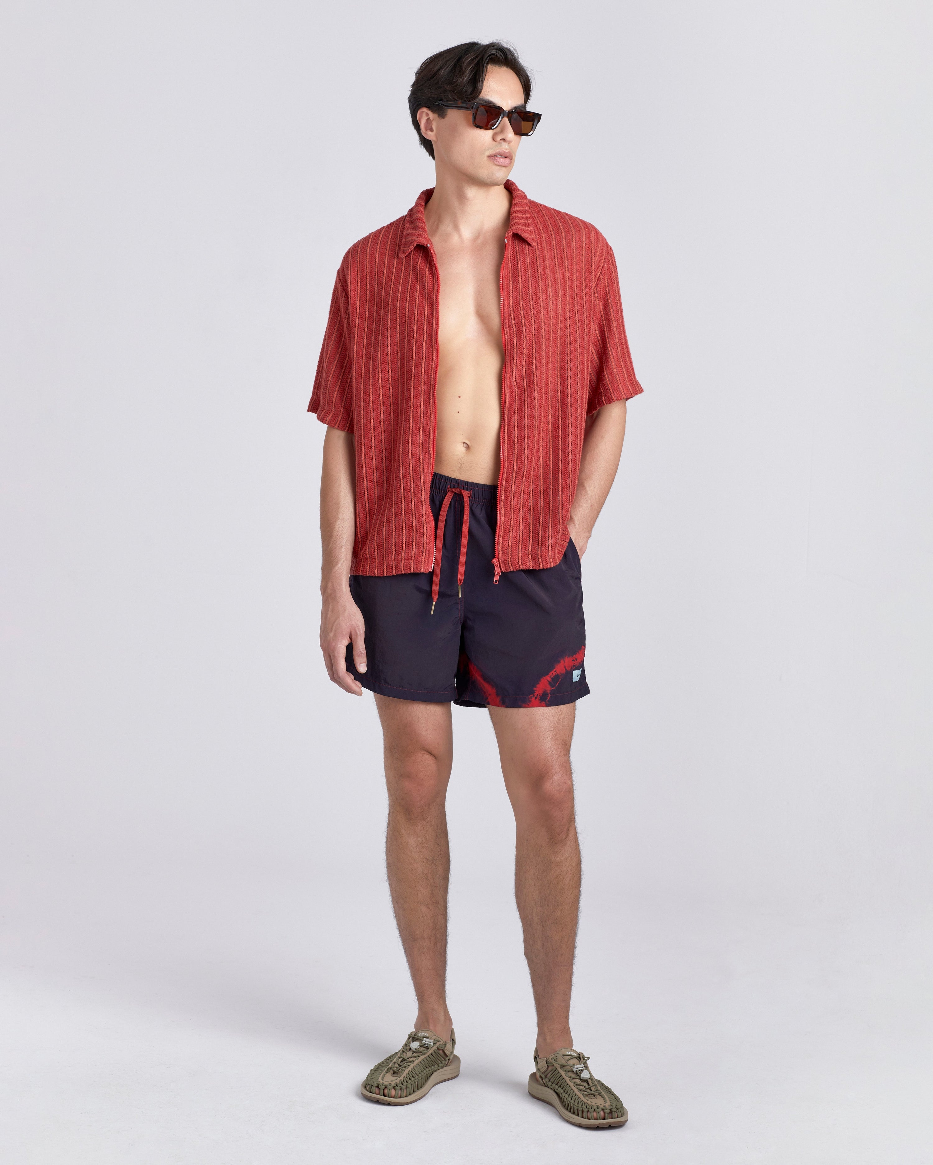 Man wearing a red shirt and black swim shorts on a white background