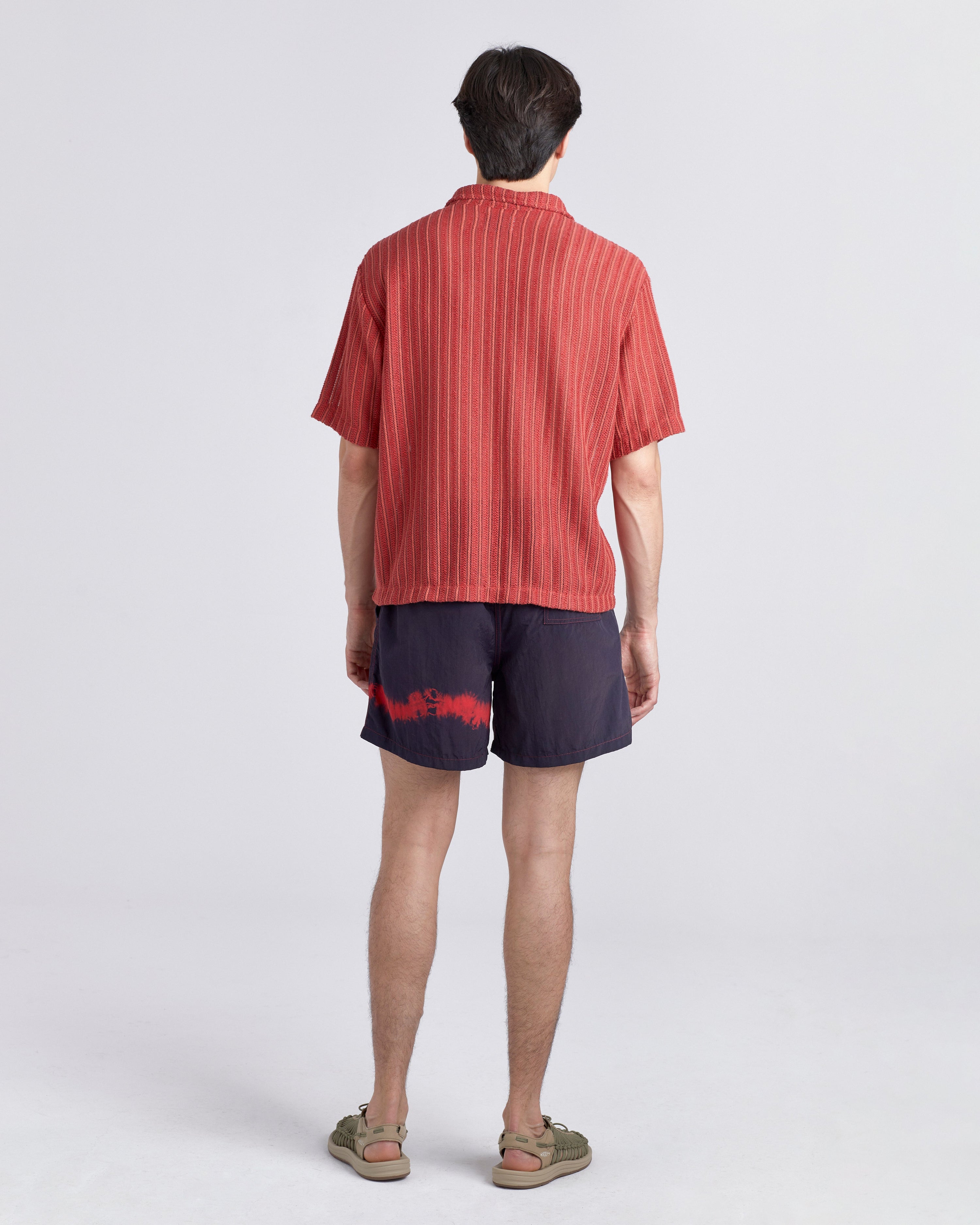Person wearing a red striped shirt and dark shorts on a white background