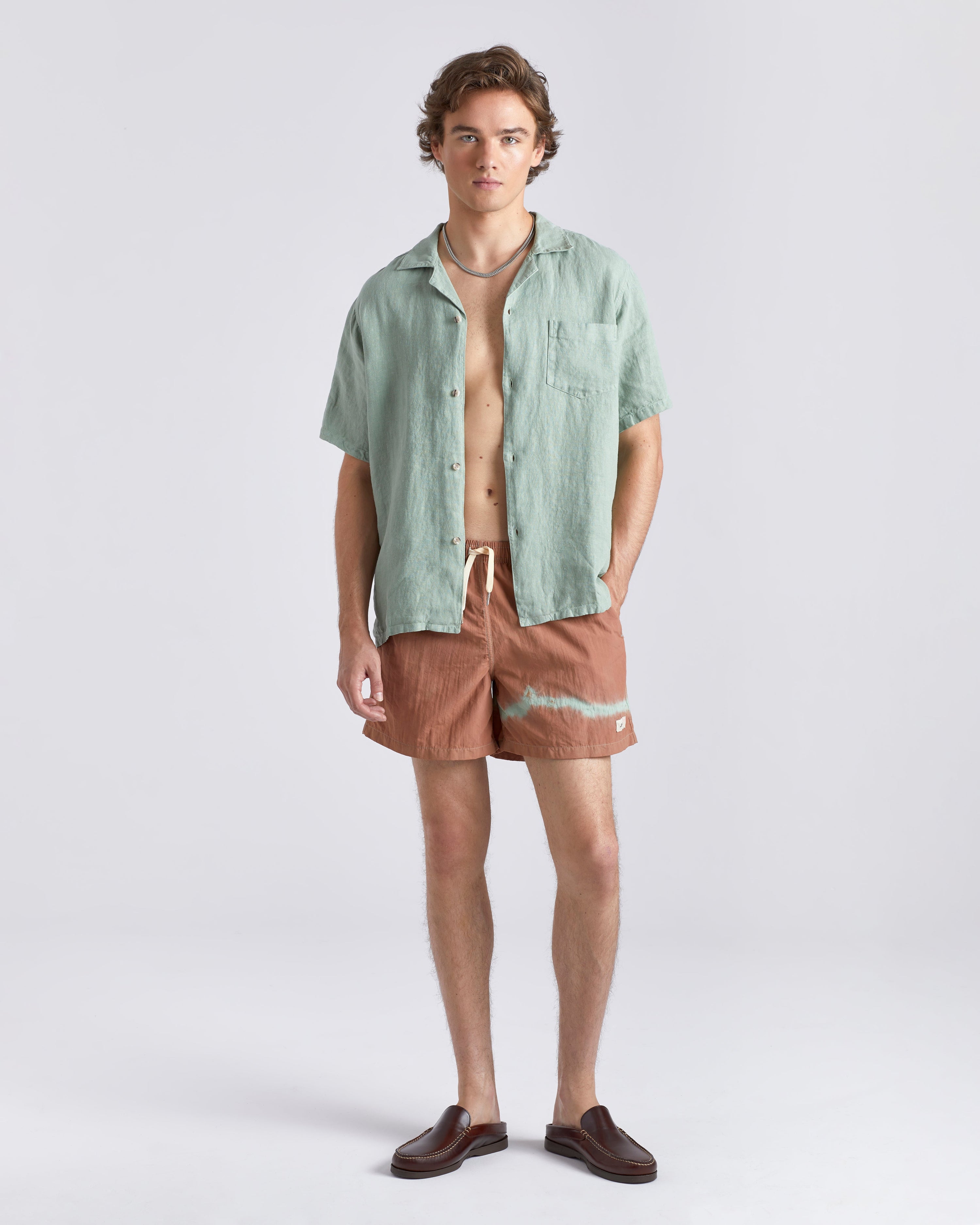 Man wearing a green shirt and brown shorts on a white background