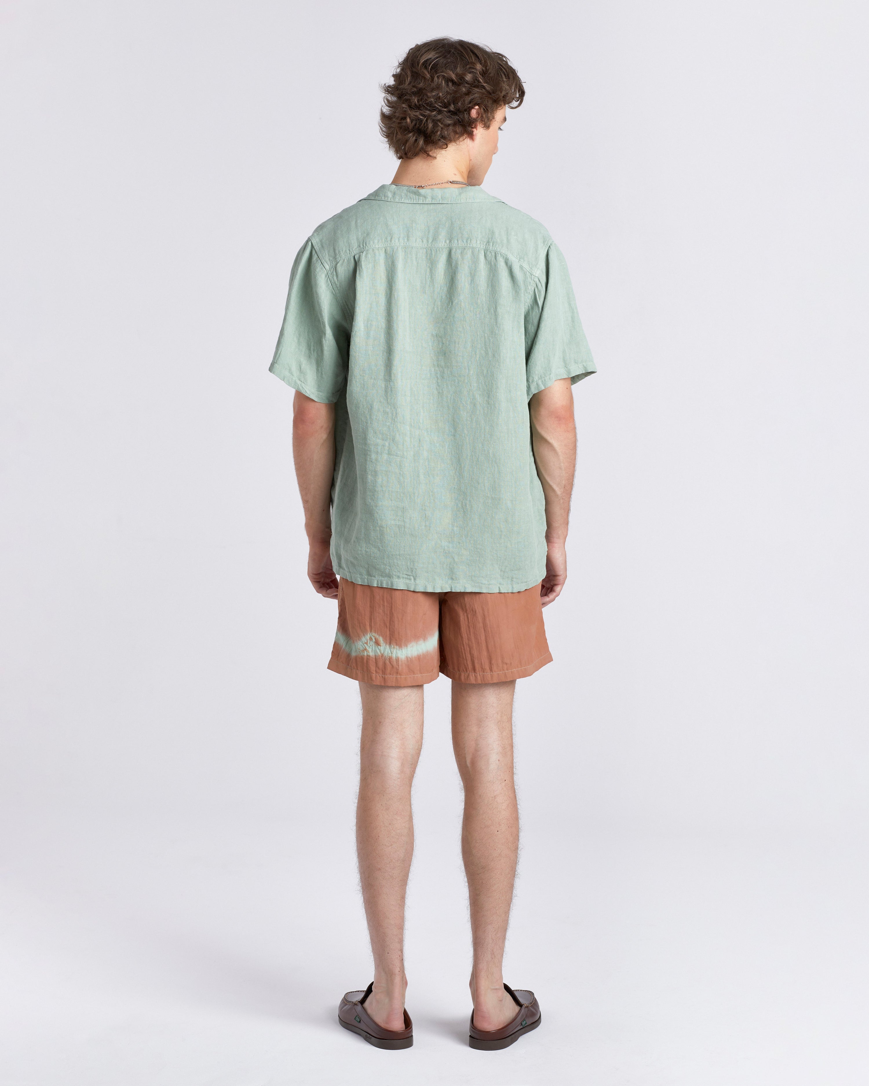 Man wearing a light green shirt and brown shorts on a white background