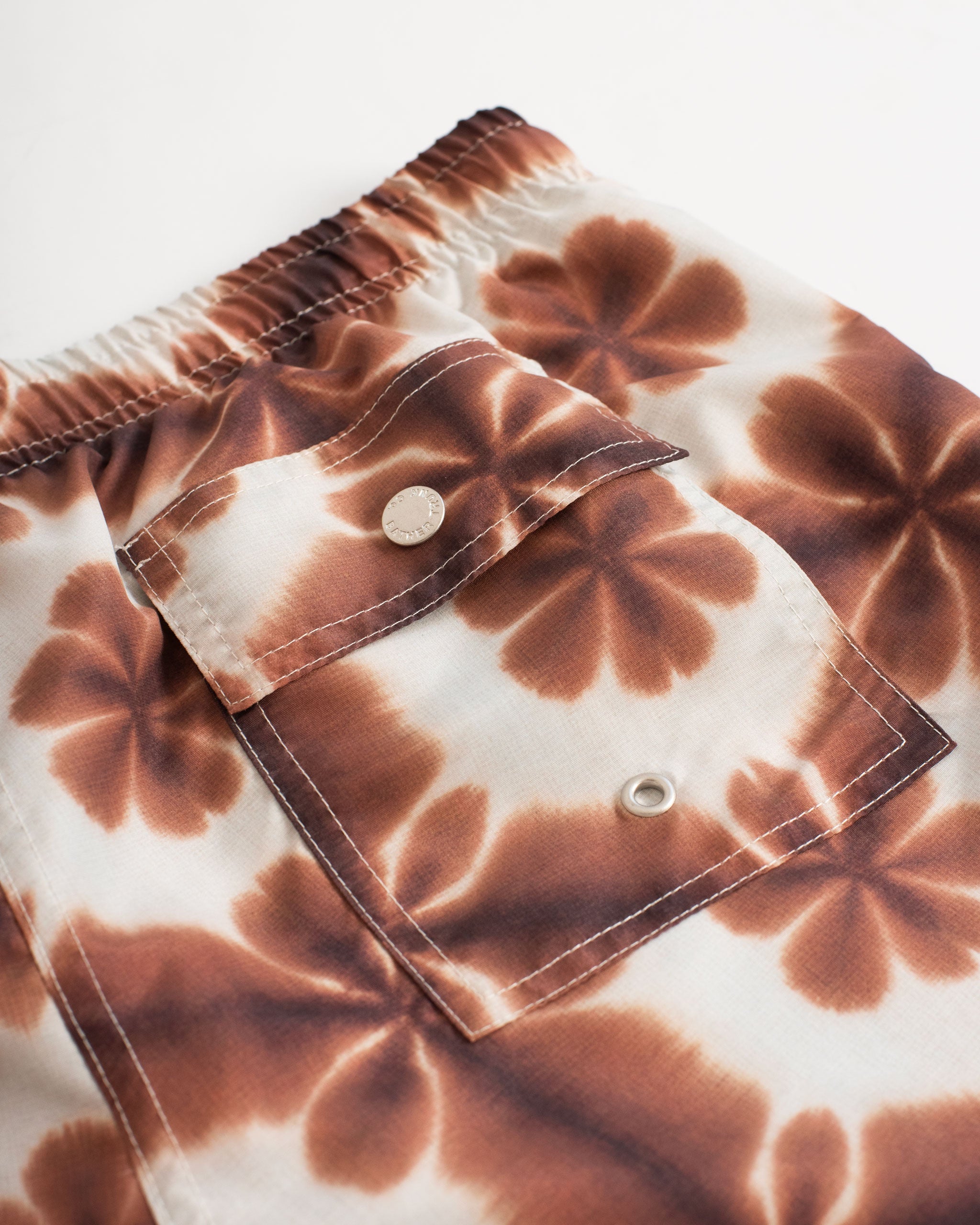 Close up of Brown swim trunk with a shibori-inspired print that looks like a kaleidoscope pattern