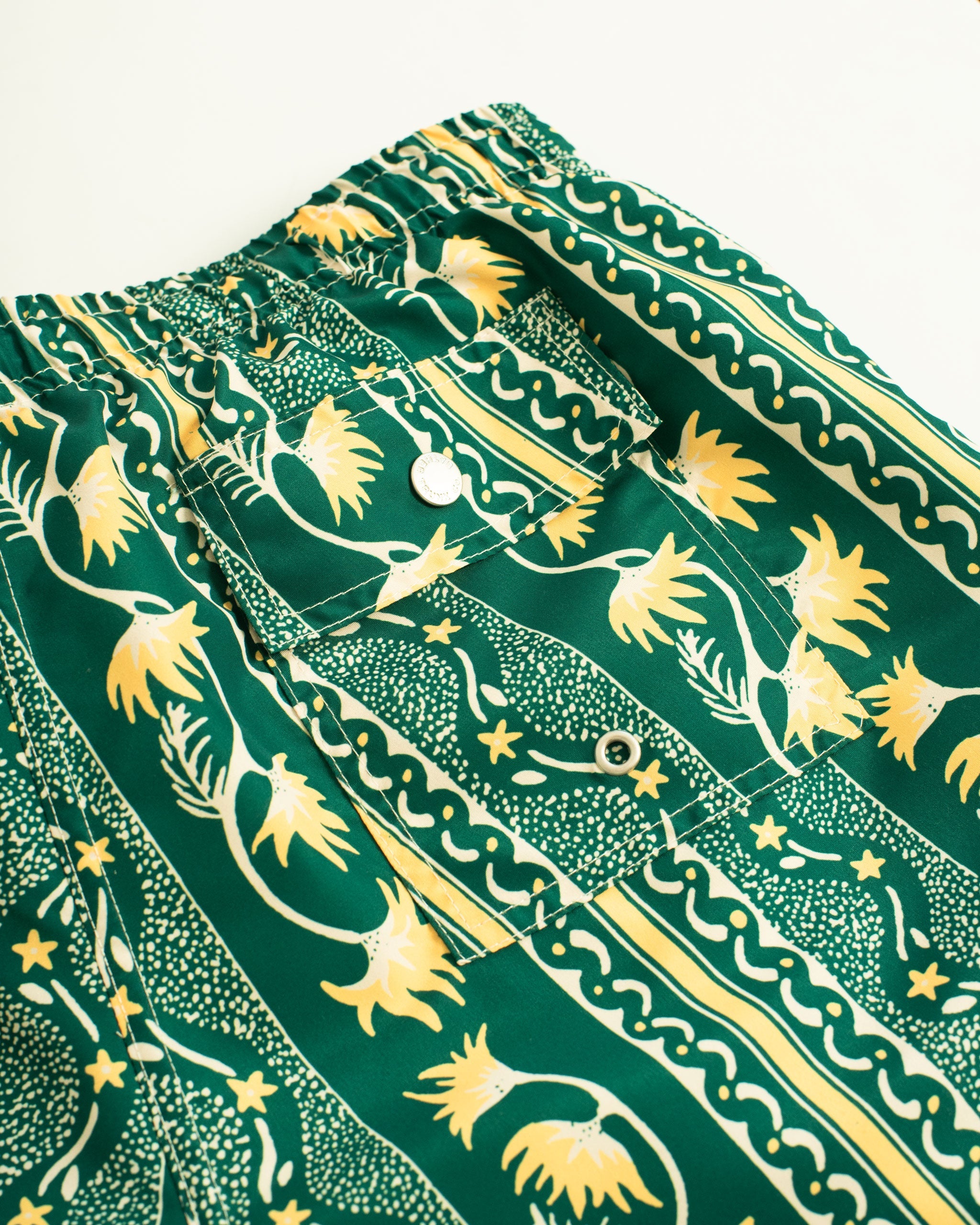 Back Pocket shot of Green swim trunk with yellow and white classic stripe features intricate mosaics of flowers, sand, and starfish