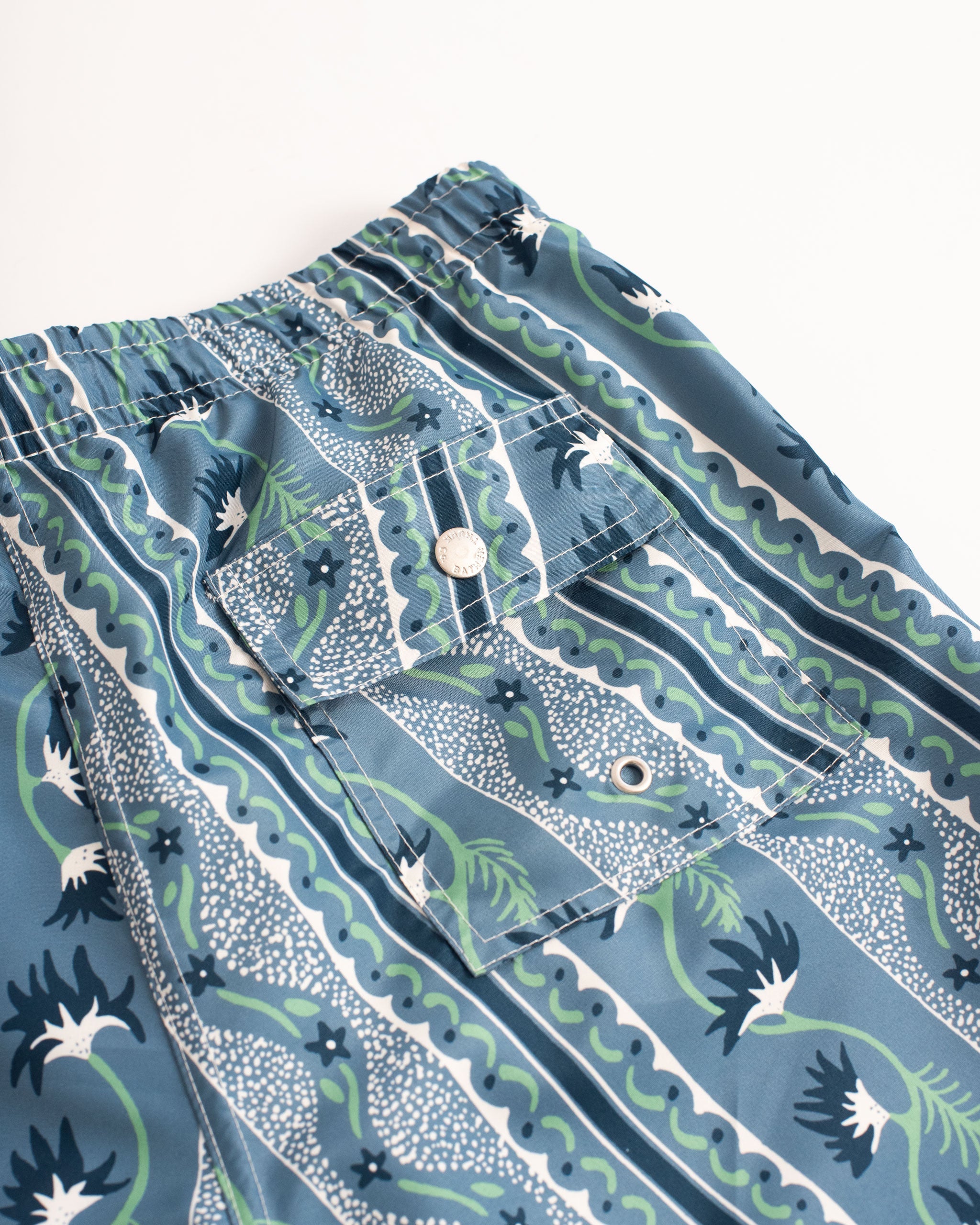 back pocket shot of Blue swim trunk with classic stripe features intricate mosaics of flowers, sand, and starfish