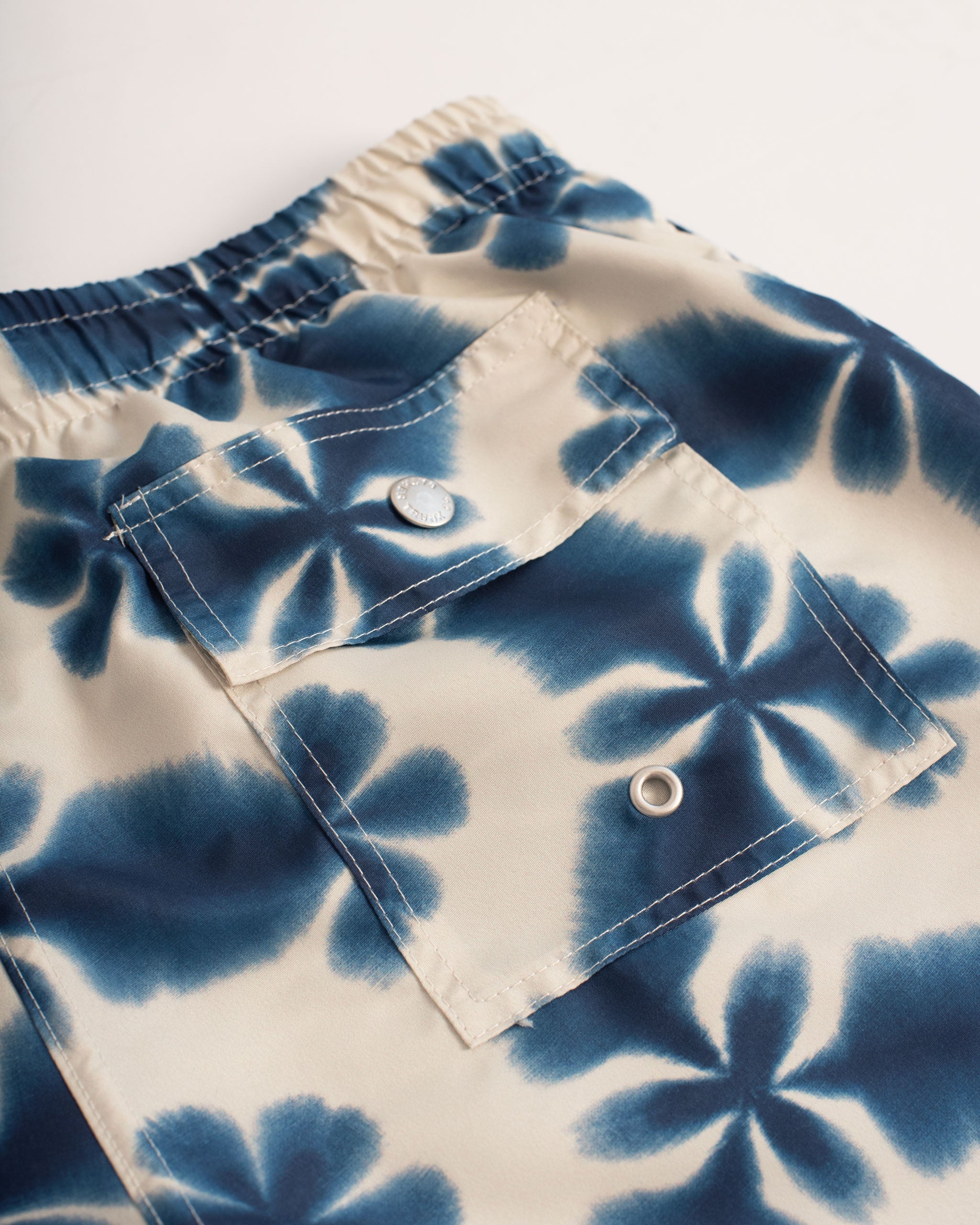 A navy swim trunk with a shibori-inspired print, similar to a kaleidoscope pattern back pocket close up