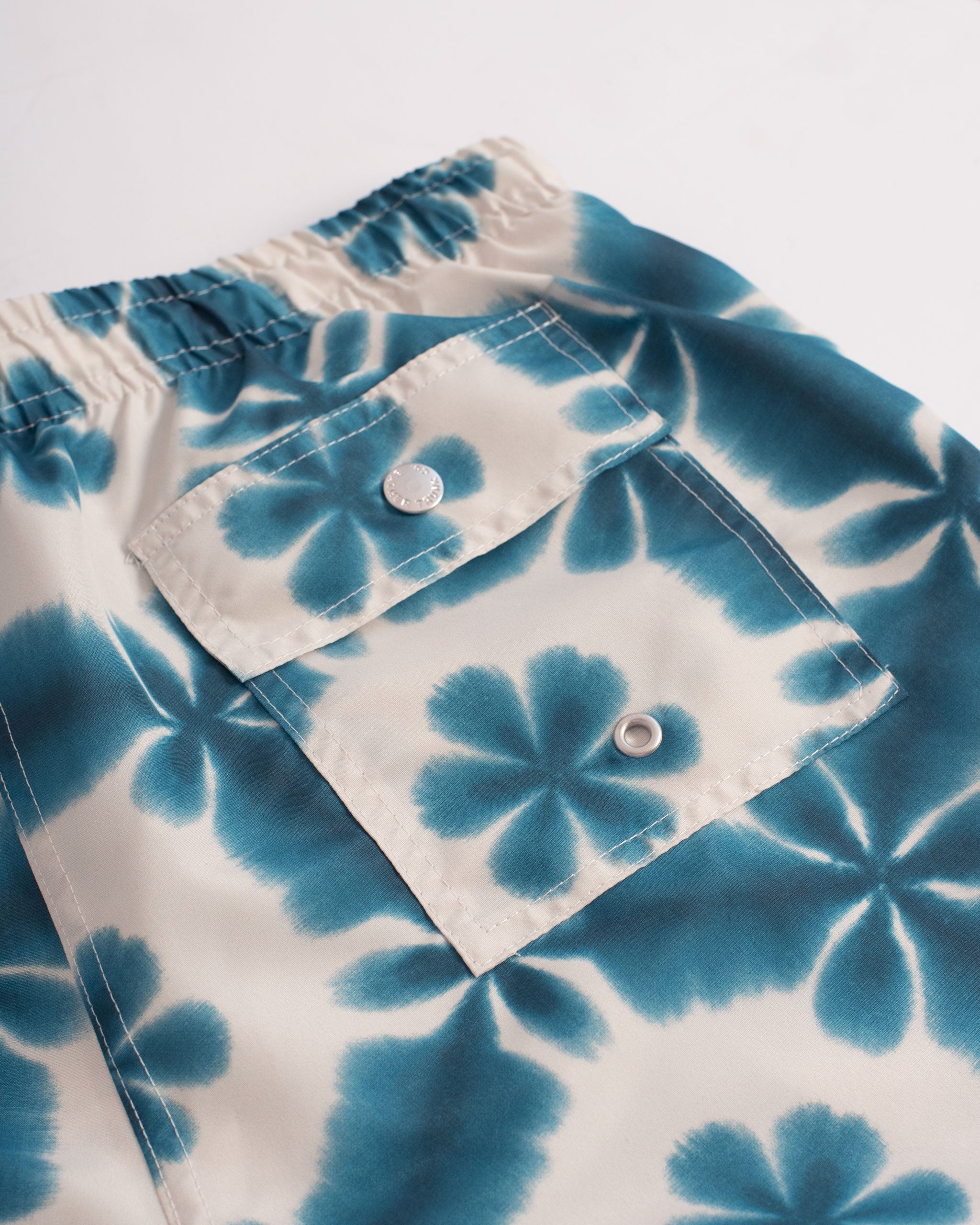 A blue swim trunk with a shibori inspired pattern, similar to a kaleidoscope back pocket close up