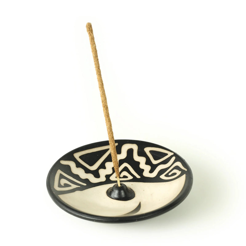 image of plate shaped incense holder, decorated with black and white designs with incense stick in the hole in the middle