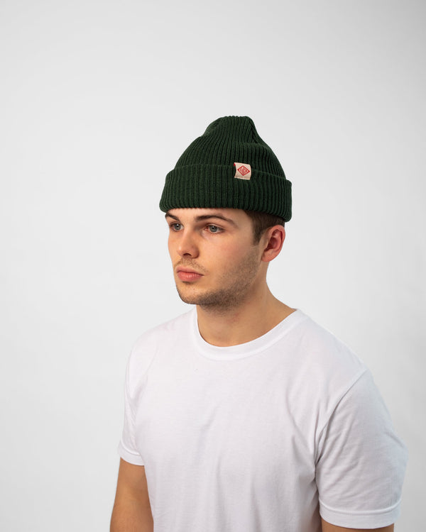 Model wearing Bather knit pine green beanie with white and red logo tag